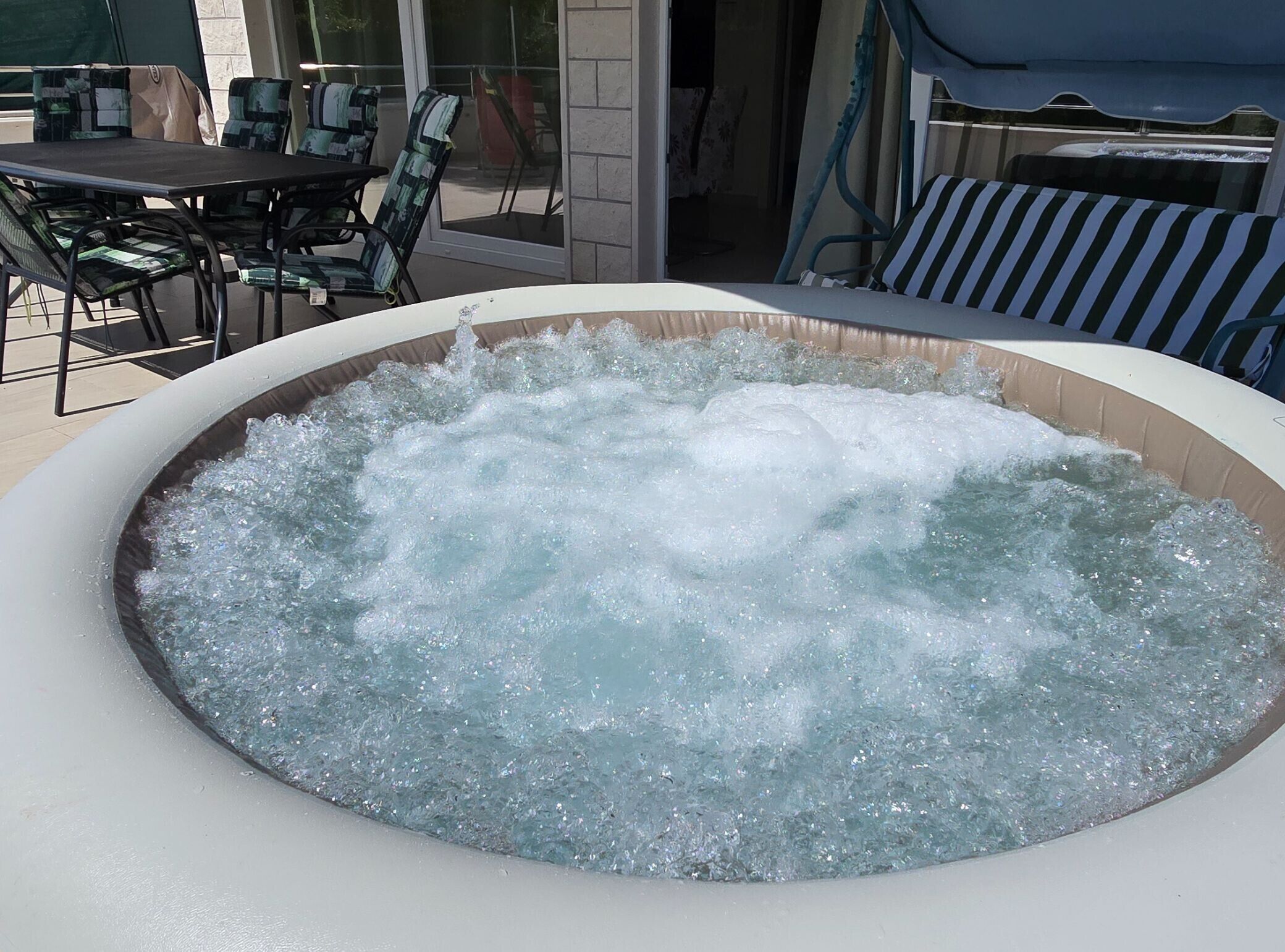 Un bain à remous dont l’eau est agitée, entouré de mobilier d’extérieur et doté d’une porte en verre donnant sur un espace intérieur.