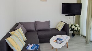 Una sala moderna con un sofá seccional gris, una mesa de centro blanca y un televisor de pantalla plana montado en la pared.