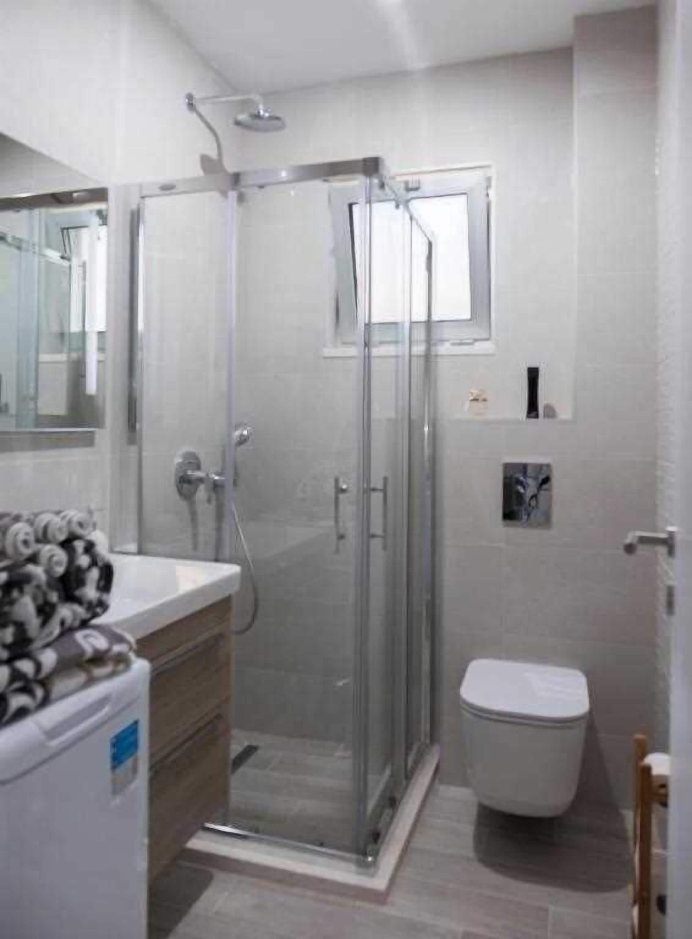 A modern bathroom with a glass-enclosed shower, a toilet, and a sink with a towel stack.