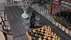 An outdoor dining area with a chessboard, wine glasses, and a bottle on a table.
