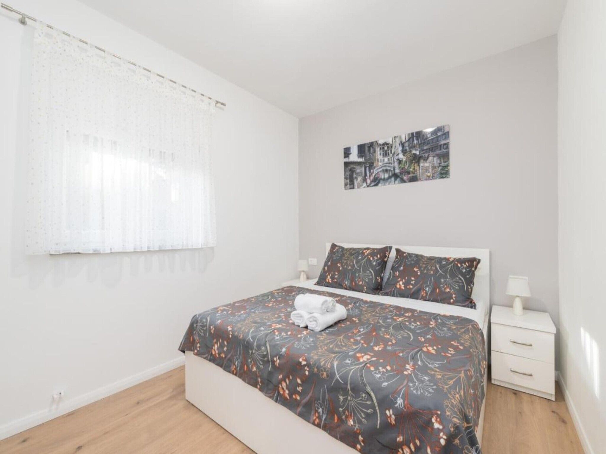 A bedroom with a bed, a nightstand, a lamp, and a window with a curtain.
