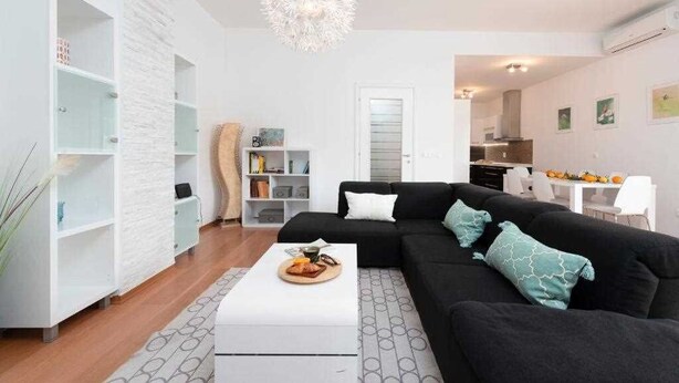 A modern living room with a black sofa, white coffee table, and a hanging light fixture. - Apartment Adrian 2BR apartment with balcony (Dubrovnik)