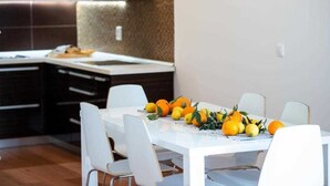 A modern kitchen with dark cabinetry, a white countertop, and a dining area with a white table and chairs. - Apartment Adrian 2BR apartment with balcony (Dubrovnik)