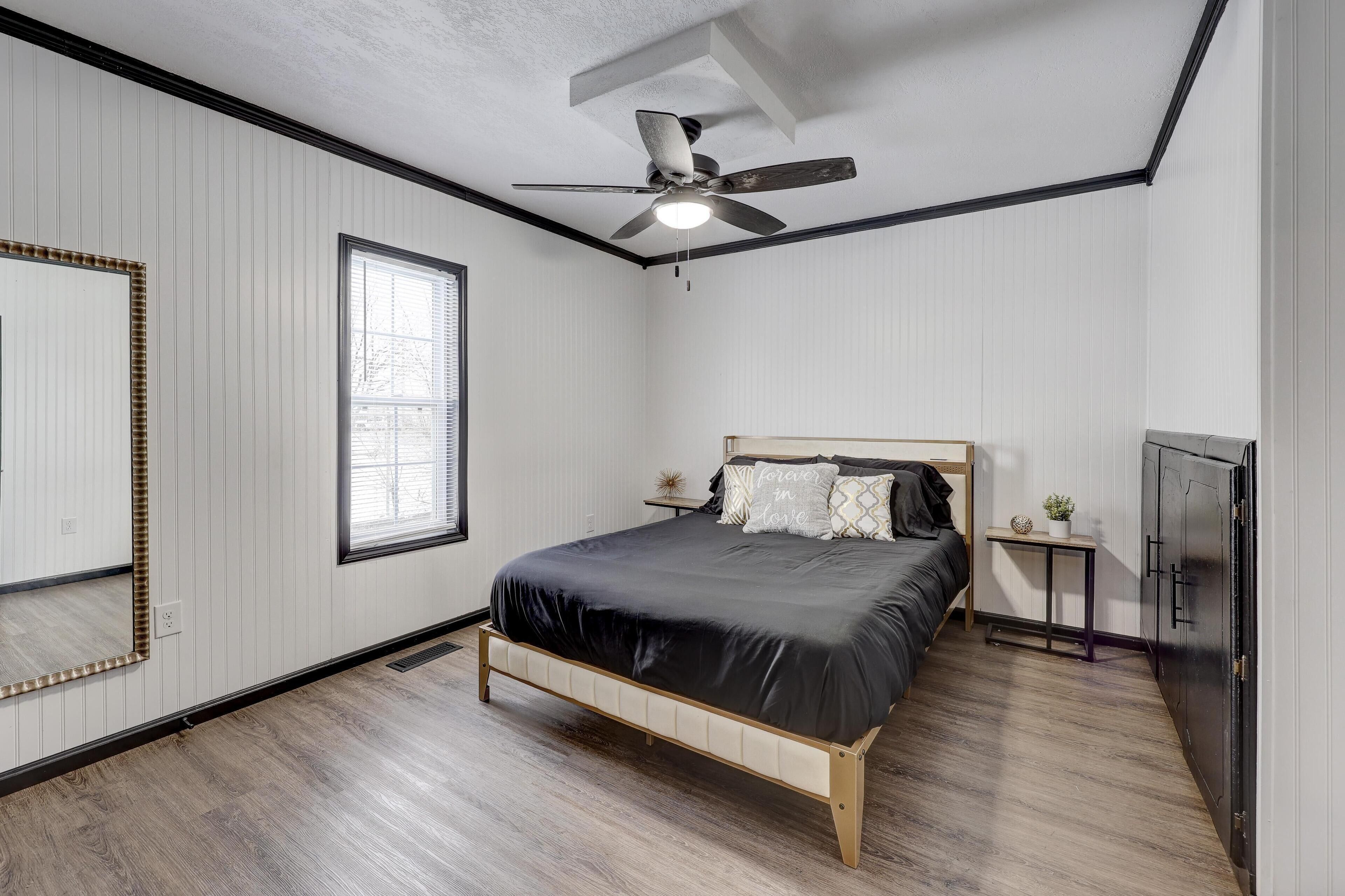 Une chambre à coucher comprenant un lit, un ventilateur de plafond, une fenêtre, un miroir et une armoire.