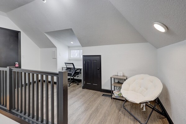 A room with a sloped ceiling, a black door, a white chair, a small table, and a window.