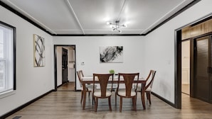 Un comedor con una mesa y sillas de madera, una lámpara en el techo y obras de arte en las paredes.