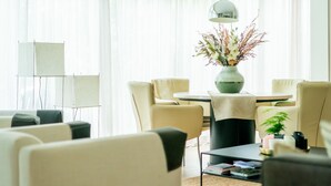 A modern living room with a round table, beige chairs, a vase with flowers, and a lamp.