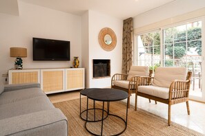 A living room with a sofa, two armchairs, a TV, a fireplace, and a large window.