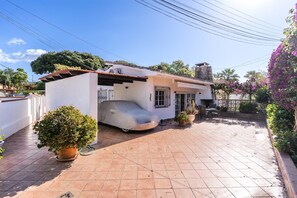 A residential property with a covered car, a patio area, and a garden with flowering plants.