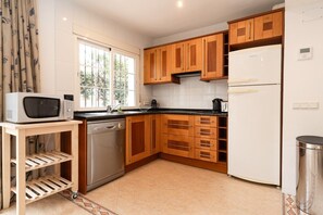 A compact kitchen with wooden cabinets, a white refrigerator, a microwave, and a dishwasher.