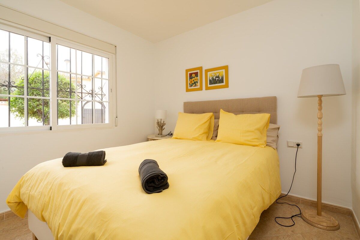 A bedroom with a bed, a bedside table, a lamp, and a window with a view.