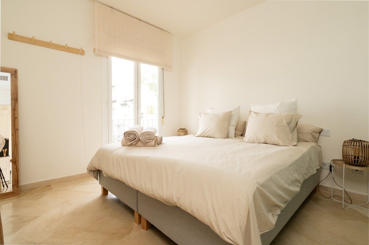 Un dormitorio con una cama, una ventana con persianas, una mesita de noche y un espejo.
