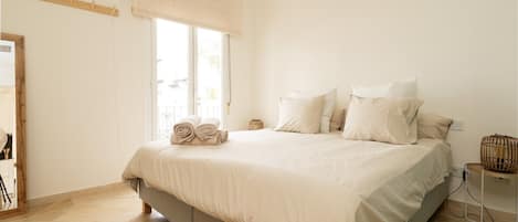 A bedroom with a bed, a window with blinds, a bedside table, and a mirror.