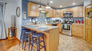 Une cuisine moderne avec des meubles en bois, un îlot central doté de tabourets, des appareils en acier inoxydable et une horloge murale décorative.