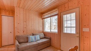 Interior de una cabaña de madera con un sofá color beige, una puerta y una ventana.