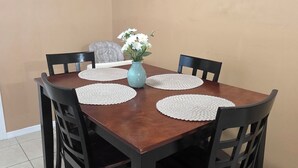 Un coin repas avec une table en bois, des chaises noires, des sets de table blancs et un vase rempli de fleurs.