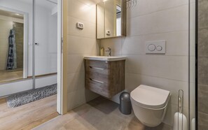 A modern bathroom with a wooden vanity, a toilet, and a shower area. - Apartment Leo (Pješčana Uvala)