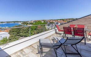A balcony with a view of a coastal town, outdoor seating, and a railing. - Apartment Leo (Pješčana Uvala)