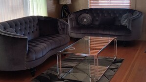 Una sala de estar con un sofá marrón oscuro, una mesa de centro de vidrio y piso de madera.