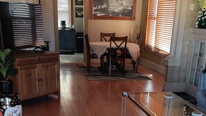 Un salón espacioso con piso de madera, una mesa de centro de vidrio, una mesa de comedor con sillas, un sofá y un espejo decorativo.