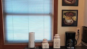 Una cocina con ventana, cafetera, basurero y un reloj en la pared.