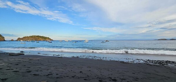 A beach with a rocky shoreline, calm sea, and boats in the distance.