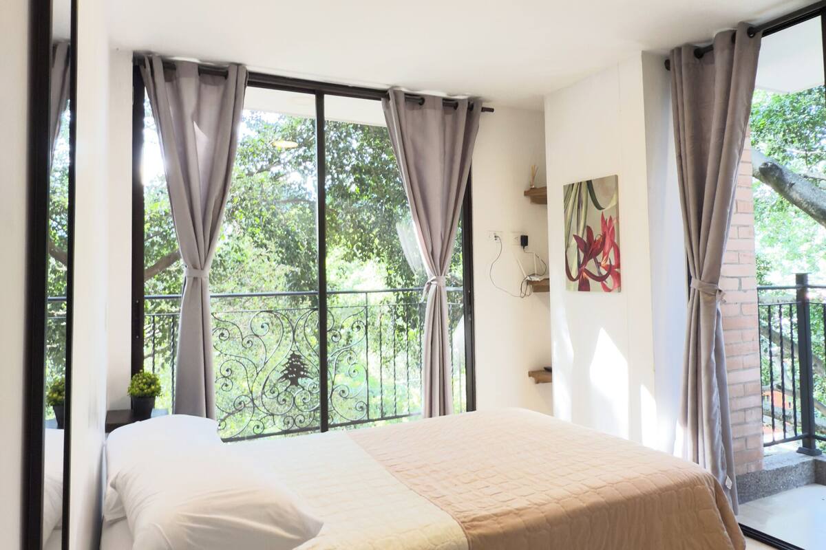 A bedroom with a bed, curtains, a window, and a balcony.