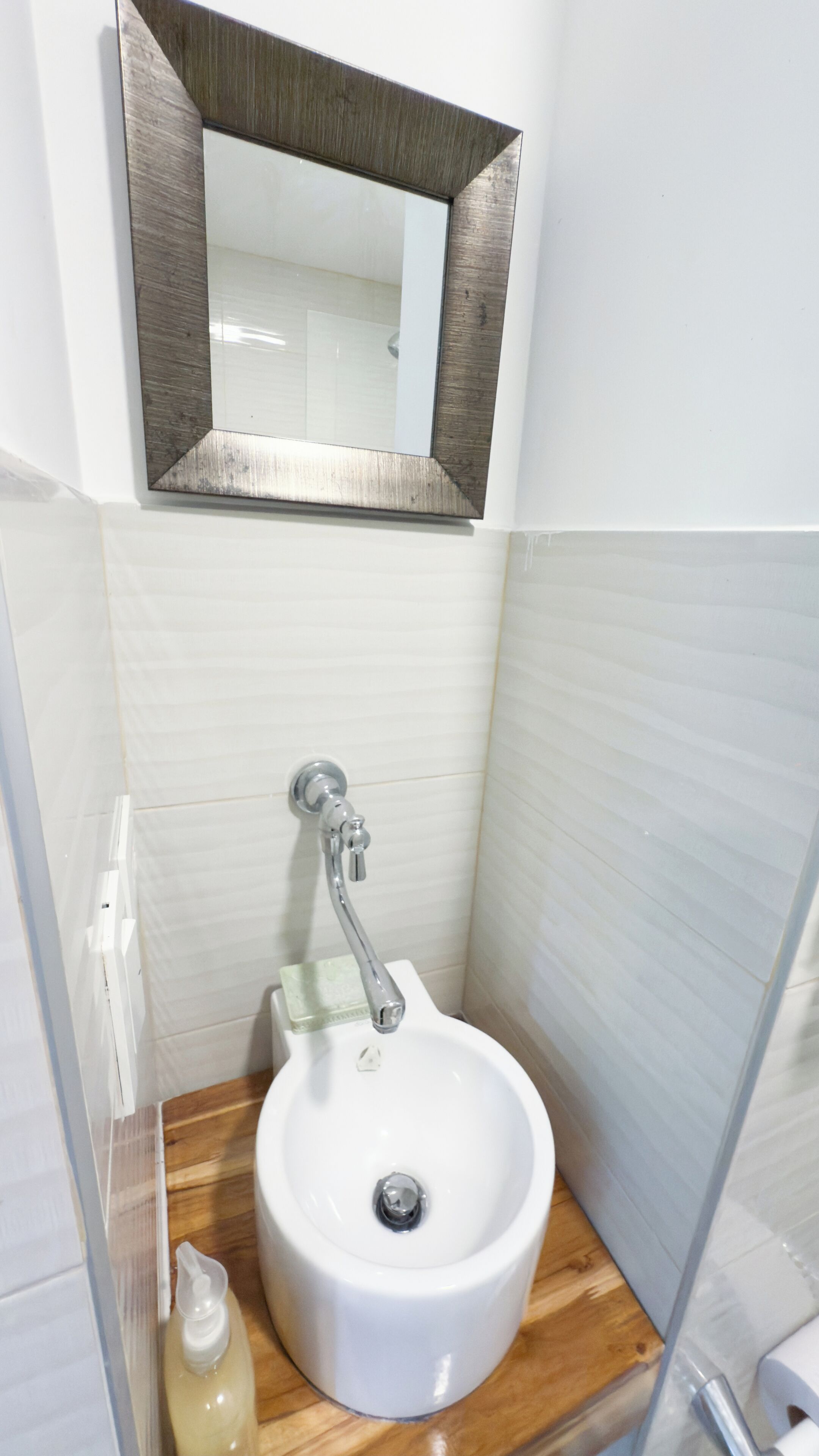 A bathroom with a white sink, wooden countertop, and a mirror above it.