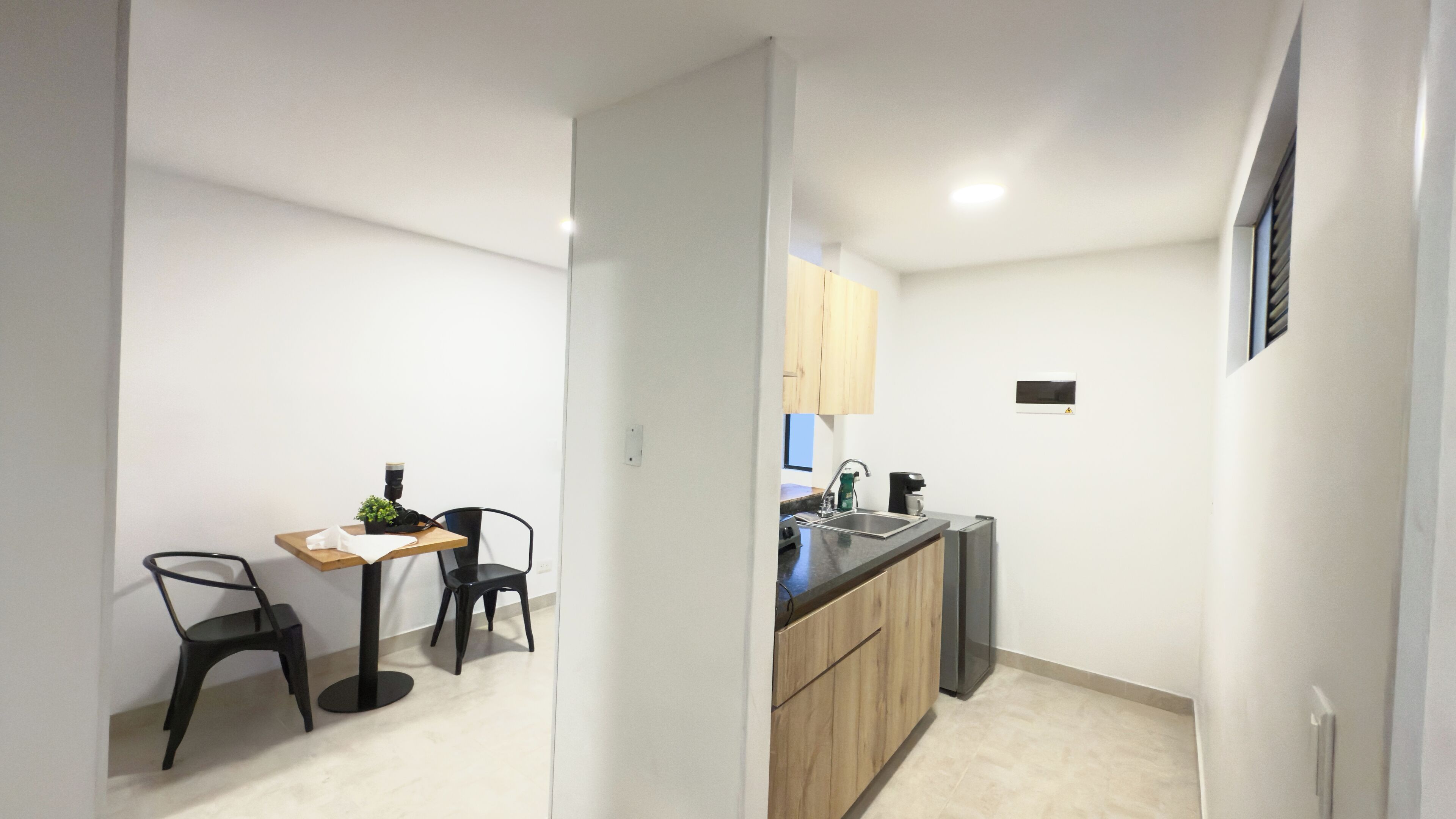 Una cocina compacta con armarios de madera, un lavamanos y una encimera. Hay un pequeño comedor con dos sillas y una mesa.