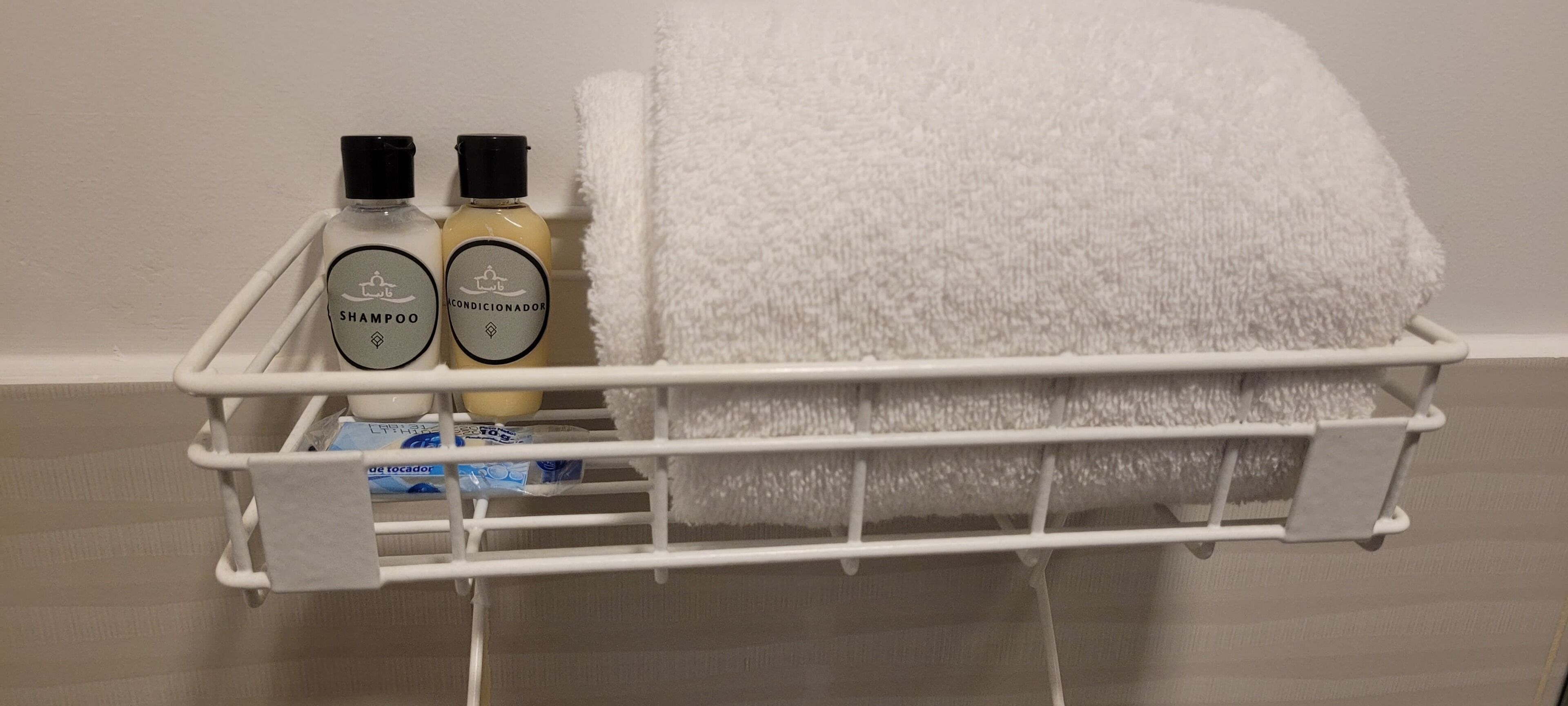 A white towel and two bottles of shampoo and conditioner on a white shelf.