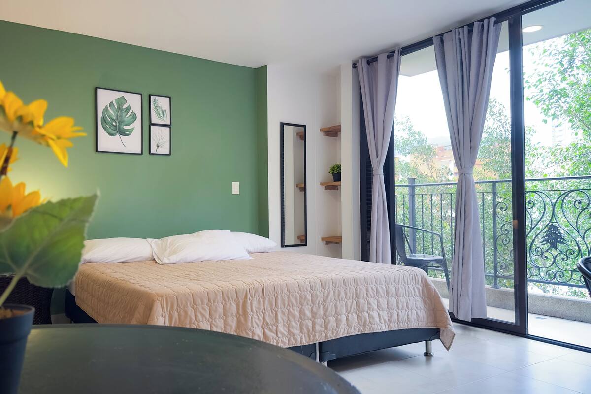 A modern bedroom with a bed, a potted plant, and a balcony with a view.