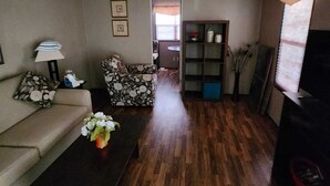 A living room with a sofa, a coffee table with flowers, a patterned armchair, a bookshelf, and a ceiling fan.