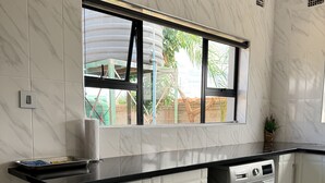 Una cocina moderna con lavadora y secadora integradas, armarios blancos, encimera negra y ventana con vistas a un jardín.
