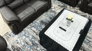 Una sala de estar moderna con dos sofás de cuero, una mesa de centro con mantel de encaje, y un comedor con una mesa y sillas grises.