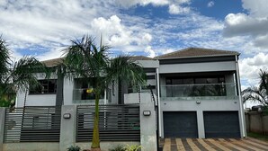 Una casa moderna de dos pisos con un camino de entrada cerrado, grandes puertas de garaje y un cielo despejado con nubes.