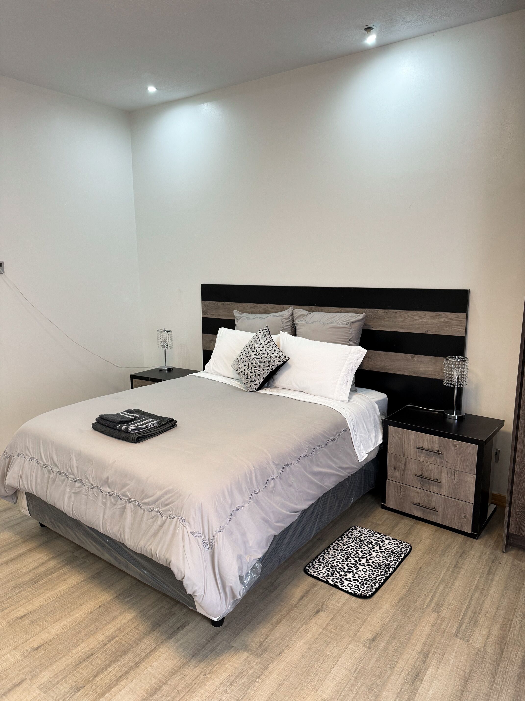 A modern bedroom with a large bed, a nightstand, a lamp, and a leopard print rug.