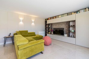 A modern living room with a sofa, a pink bean bag, a TV, and a bookshelf.