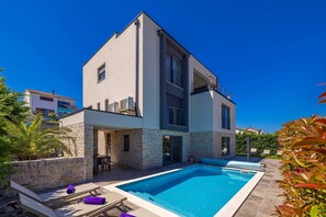 Una casa moderna de dos pisos con piscina, paredes de piedra y balcón.