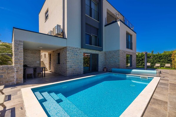 A modern two-story house with a swimming pool, stone walls, and a balcony.
