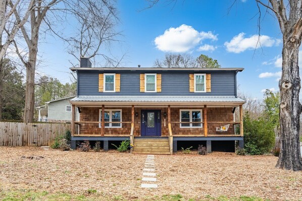 A two-story house with a front porch, a wooden deck, and a stone pathway leading to the door.