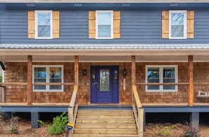 A two-story house with a wooden exterior, a blue front door, and a covered porch with steps leading to the entrance.