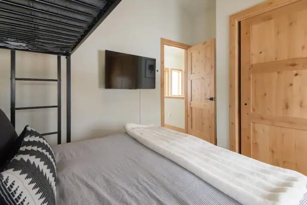 Un dormitorio con una cama, un televisor montado en la pared y una puerta de madera.