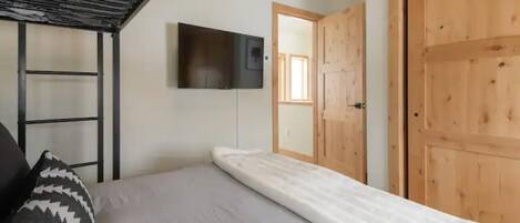 Un dormitorio con una cama, un televisor montado en la pared y una puerta de madera.