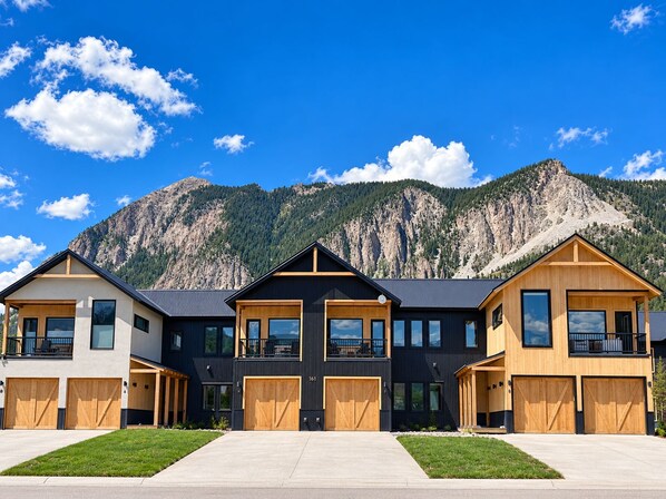 A row of modern houses with large garage doors, set against a mountainous backdrop.