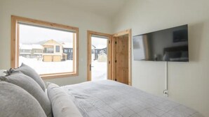 A bedroom with a bed, a TV mounted on the wall, and a large window. - Modern Mountain Retreat, 360'Views,Minutes to Trails (Crested Butte)