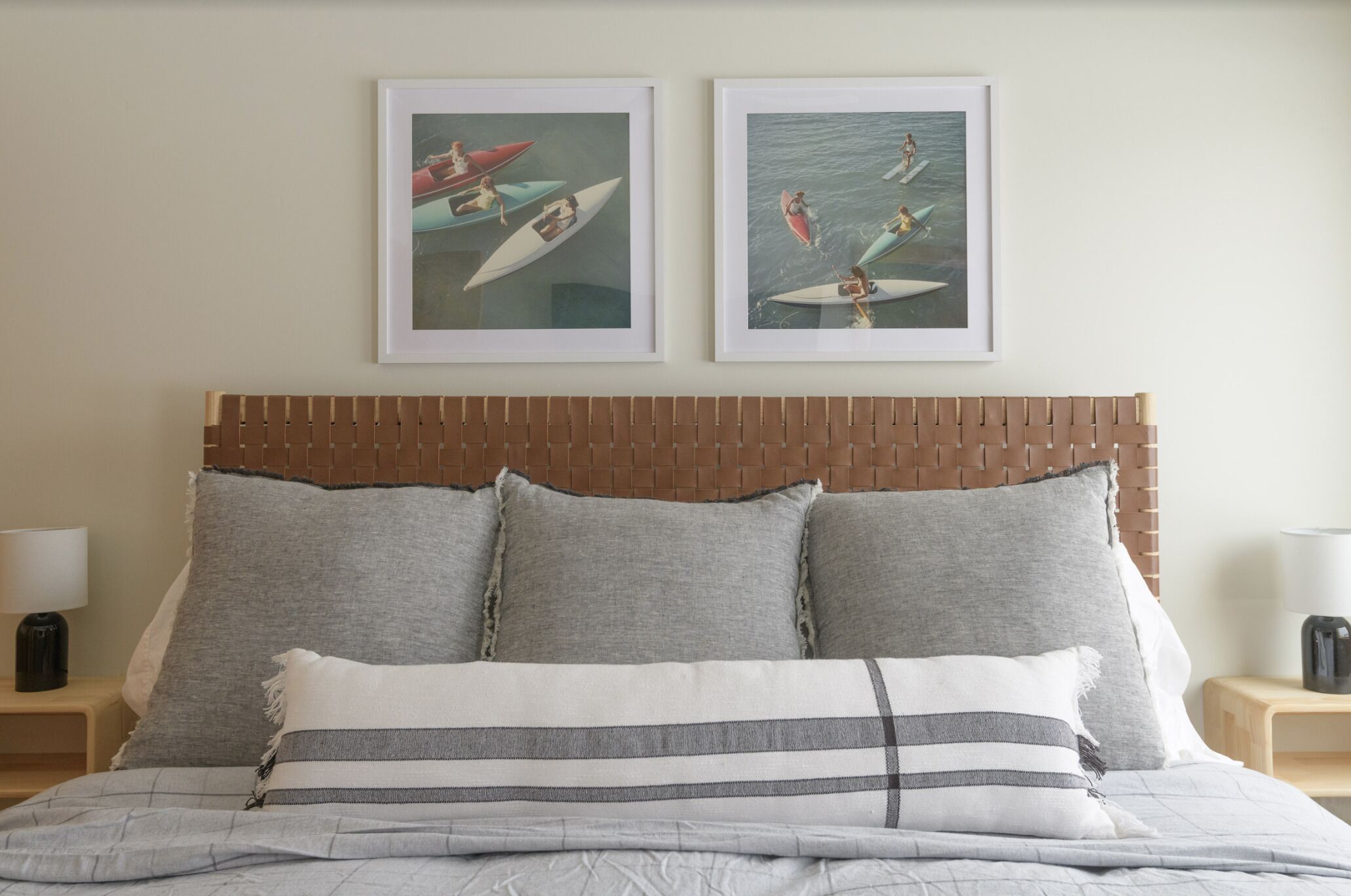 A neatly made bed with grey and white bedding, two framed pictures of surfers on the wall, and a wooden headboard.