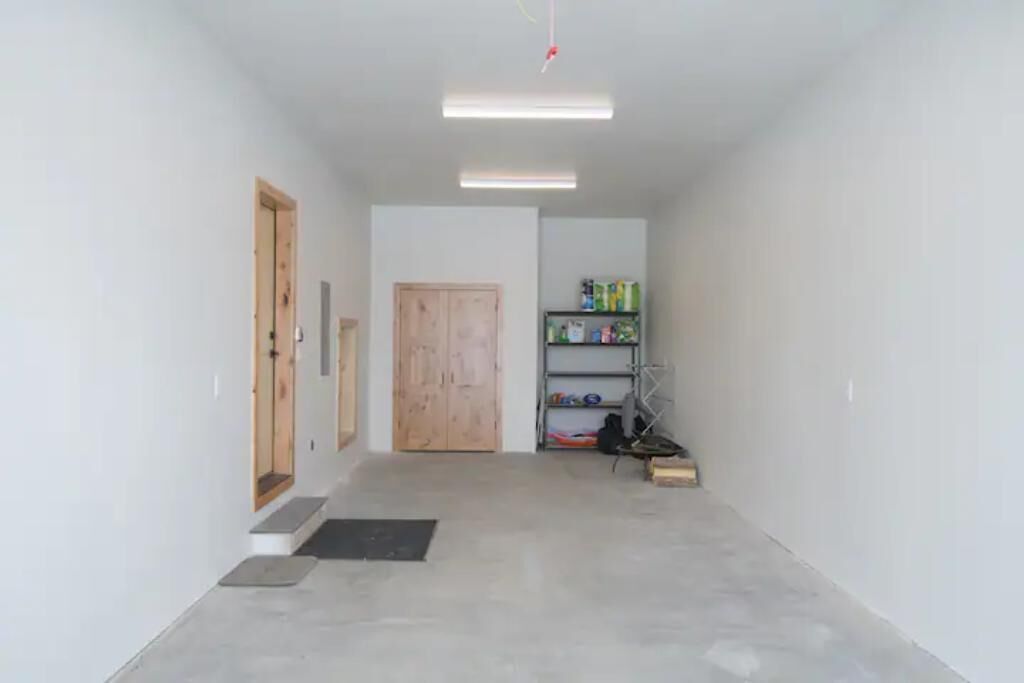 A narrow hallway with a wooden door, a shelf with various items, and a small step leading to a door.
