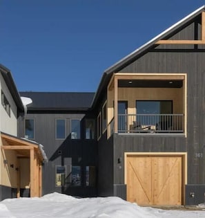 A modern two-story house with a dark exterior, a wooden balcony, and a garage. - Modern mountain retreat with heated garage near town! (Crested Butte)