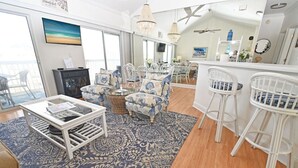 Amplia sala de estar con un ventanal grande, chimenea y comedor con sillas blancas y una mesa.