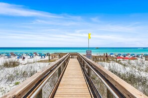 A wooden boardwalk leading to a beach with umbrellas and people. - Sandpiper Cove Unit 2065 1 Bedroom With FREE Beach Set Up! Destin, FL (Destin)